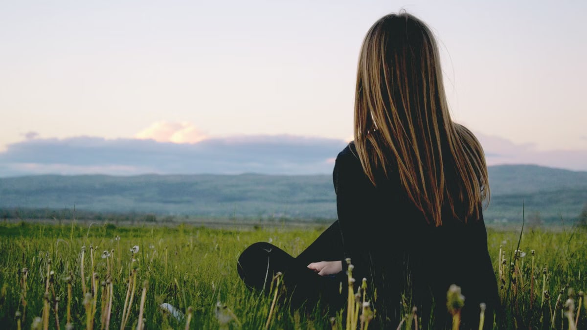 Woman enjoying peace in a lush green field with a scenic mountain view during sunset.